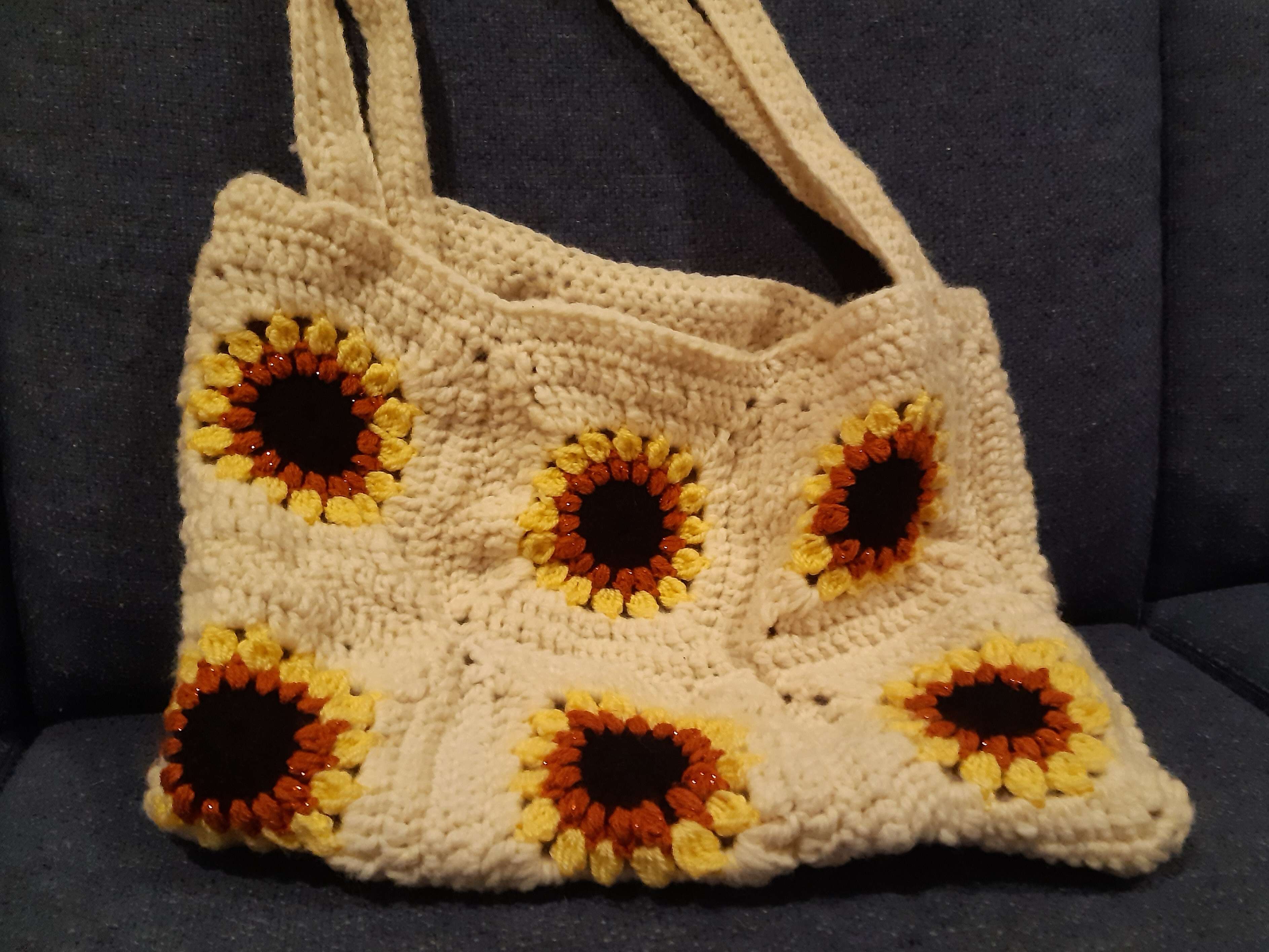 a white crocheted bag made with granny squares that each depict a sunflower.