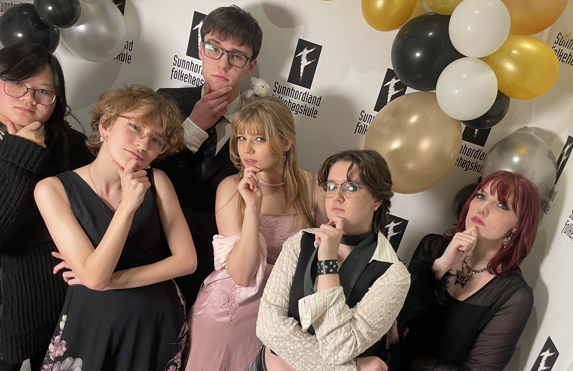 Six people dressed formally posing for the camera, balloons in the background.